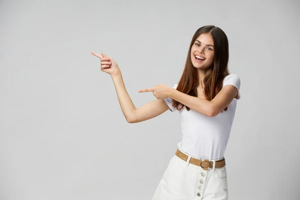 Usmívající se žena v bílém tričku a trenýrkách ukazuje prsty na stranu kopírovat prostor — Stock fotografie