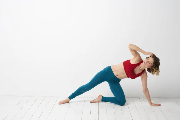 En kvinna i blå jeans tränar yoga på en ljus bakgrund inomhus och en smal figur i gymnastik — Stockfoto