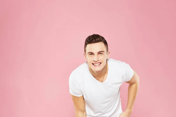 Vrolijke knappe man in wit t-shirt emoties roze geïsoleerde achtergrond — Stockfoto