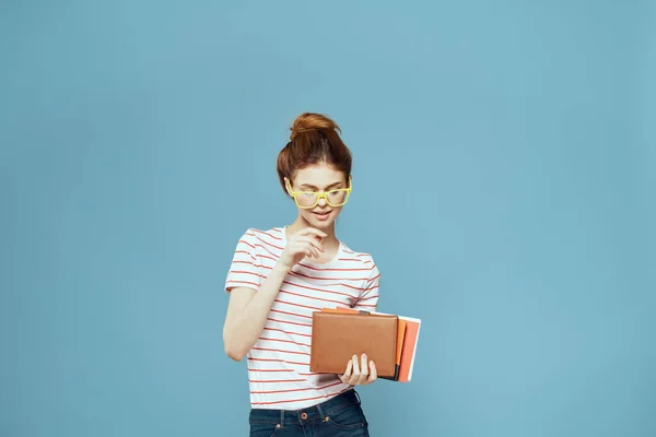Kvinna student med böcker i händerna på en blå bakgrund och gula glasögon modell frisyr beskärd vy — Stockfoto