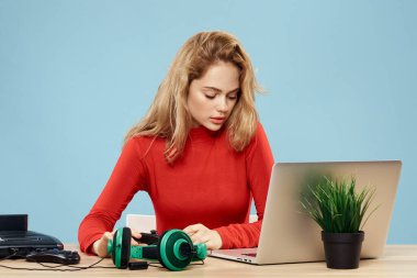 Dizüstü bilgisayar kulaklığının önündeki masada oturan bir kadın çevrimiçi yaşam tarzı mavi arka planda oynuyor.