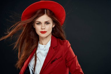 Kırmızı dudaklı güzel bir kadın ceketinde şapkası olan zarif stil cazibesi koyu tenli arka planda.