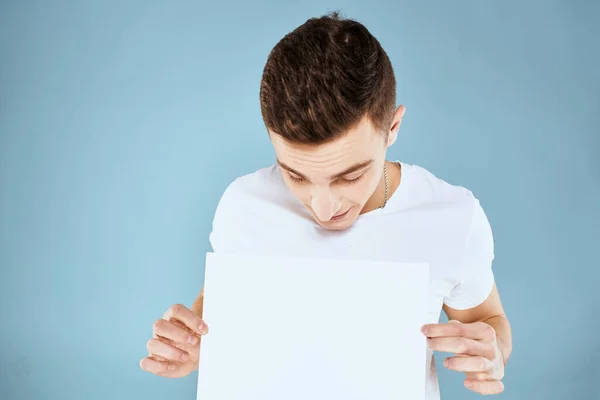 A man in a white t-shirt holds in his hands a sheet of paper emotions cropped view of a blue background Copy Space — Stock Photo, Image