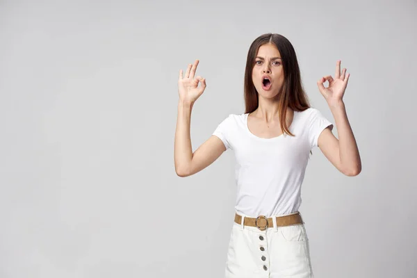 Egy energikus nő nyitott szájjal pozitív gesztusokat mutat, kezével a könnyű háttér — Stock Fotó