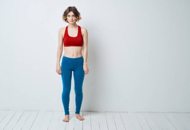 Mavi kotlu ve kırmızı tişörtlü bir kadın açık arkaplanda spor yapmaya gider.