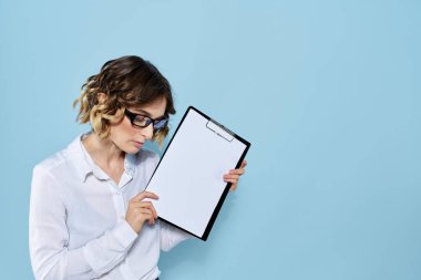 Mavi arka planda bir klasörde evrakları olan ve yüzünde açık renk gözlüklü bir iş kadını.
