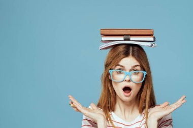 Kafası üzerine kitapları olan kız öğrenci. Bilim eğitimi almış. Mavi arka plan duyguları elleriyle hareket ediyor.