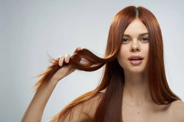 Hübsche rothaarige Frau hält ihre Haare mit Händen, die nackte Schultern pflegen, heller Hintergrund — Stockfoto