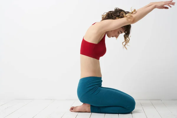 Het meisje is bezig met yoga op een lichte achtergrond rood T-shirt gesticulating met zijn handen — Stockfoto