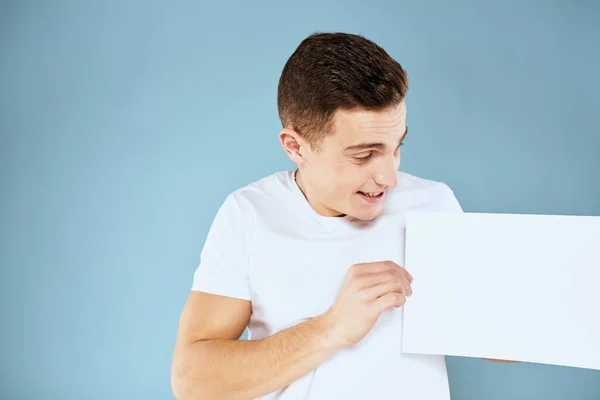 Man holding a sheet of paper in his hands white t-shirt cropped view blue background — Stock Photo, Image