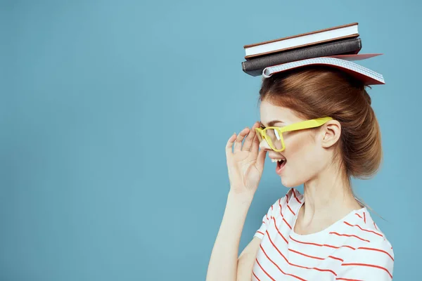 Étudiante avec des livres sur la tête et des lunettes jaunes sur fond bleu vue recadrée — Photo