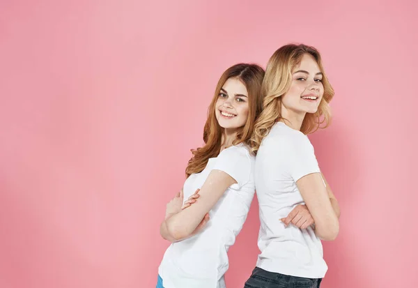 Две девушки в белых футболках стоят спиной друг к другу на розовом фоне — стоковое фото