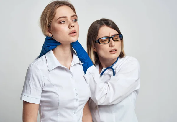 Eine Krankenschwester in blauen Handschuhen untersucht eine Patientin im weißen T-Shirt vor hellem Hintergrund. — Stockfoto
