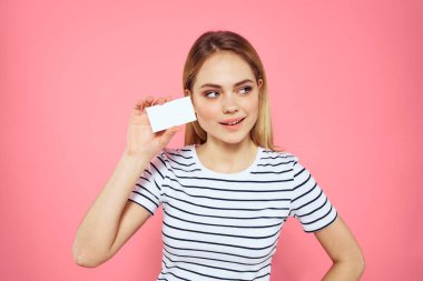 Elinde kartvizit olan bir kadın çizgili bir tişört pembe arka plan fotokopi alanı reklamı