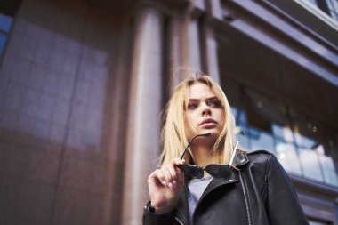 Binanın yakınında deri ceketli ve güneş gözlüklü şık bir kadın. 