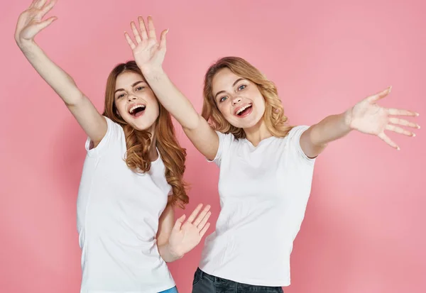 Dwie emocjonalne dziewczyny w t-shirt zabawy styl życia studio różowy tło — Zdjęcie stockowe