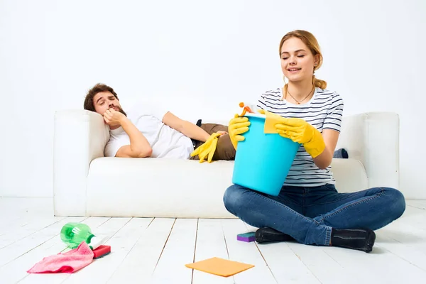 The husband lies on the couch while his wife cleans up the interior work — Stock Photo, Image