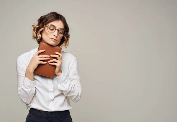 Jolie femme en lunettes et une chemise blanche sur fond gris avec un livre dans les mains — Photo