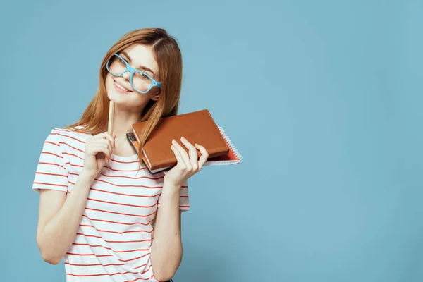 Chica en gafas de moda con cuadernos en las manos sobre un fondo azul recortado vista Copiar espacio —  Fotos de Stock