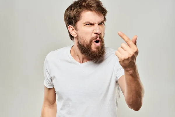 Skäggig man gestikulerar med händerna i en vit t-shirt aggression ljus bakgrund — Stockfoto