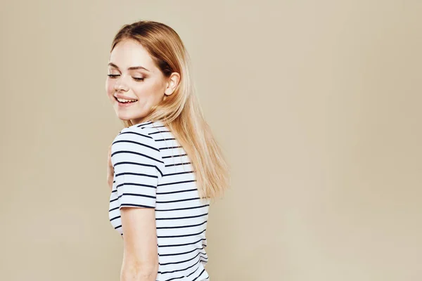 Симпатична блондинка смугаста футболка посмішка спосіб життя бежевий студійний фон — стокове фото