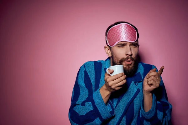 Homem com uma xícara de chá na mão e com uma máscara rosa no rosto em um fundo rosa vista cortada — Fotografia de Stock