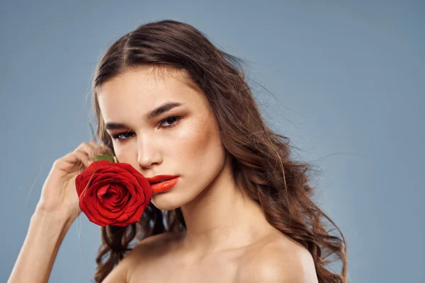 Portrait d'une femme avec une rose rouge dans les mains sur un fond gris épaules nues maquillage du soir — Photo