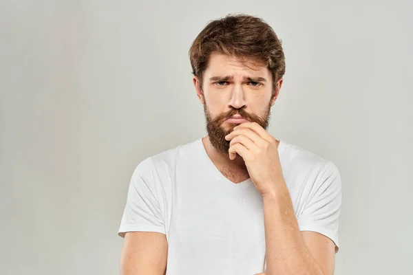 En man i vit t-shirt med skägg känslor missnöjd ansiktsuttryck ljus bakgrund — Stockfoto