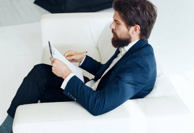 Takım elbiseli bir iş adamı beyaz bir kanepede oturur.