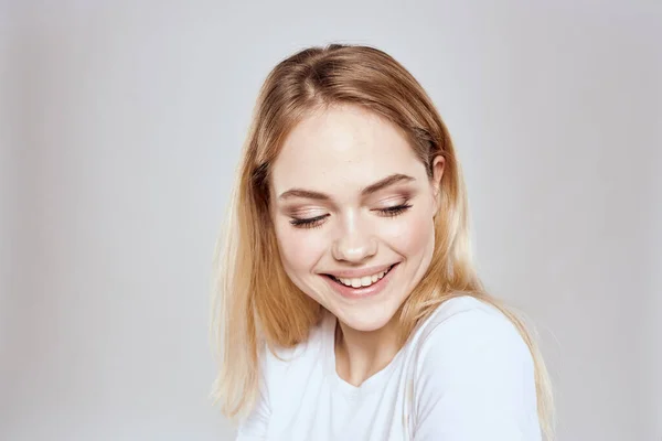 Glad blond i en vit t-shirt gest med händerna ljus bakgrund — Stockfoto