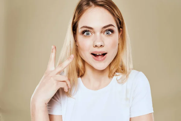 Mulher loira alegre em um branco gestos camiseta com suas emoções da mão fundo bege — Fotografia de Stock