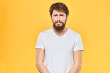 Sakallı adam duyguları, yüz ifadesi, beyaz tişört, sarı arka plan.