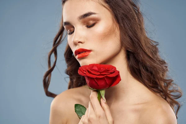 Portrait de femme avec rose rouge près du visage sur fond gris et maquillage cheveux bouclés — Photo