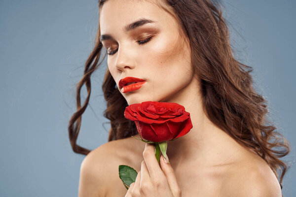 Woman portrait with red rose near the face on gray background and makeup curly hair