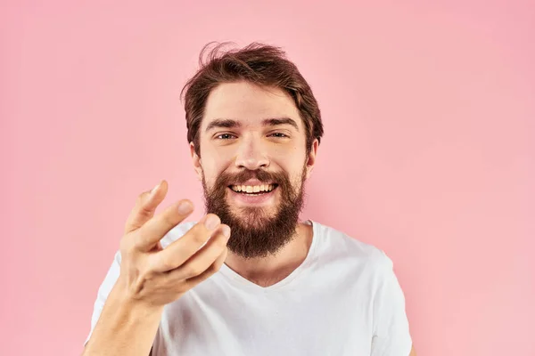 하얀 티셔츠를 입고 손에 감정 표현을 하고 있는 남자가 핑크 색 배경을 보고 있다. — 스톡 사진