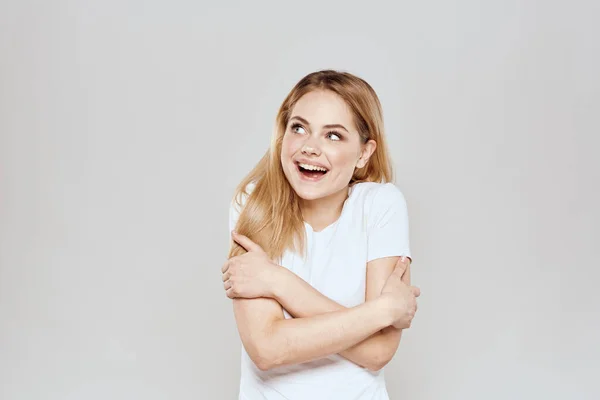 Munter blondine i en hvid t-shirt gesturing med hænderne lys baggrund - Stock-foto