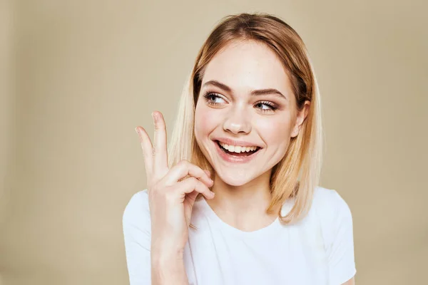 Allegro donna bionda in un bianco gesti T-shirt con le sue emozioni mano sfondo beige — Foto Stock