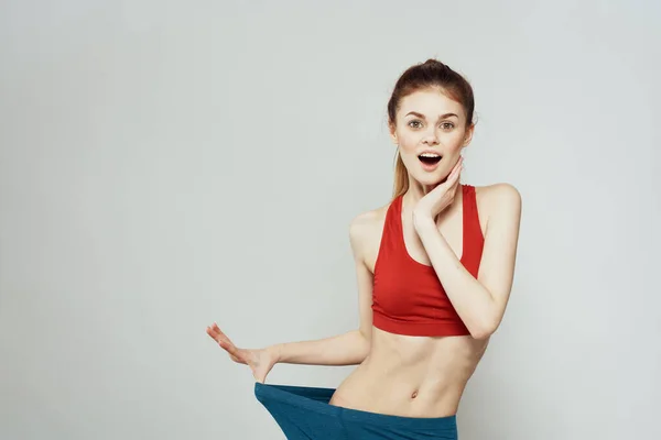 Una mujer con una camiseta roja sobre un fondo claro se dedica a gestos de fitness con las manos una figura delgada —  Fotos de Stock