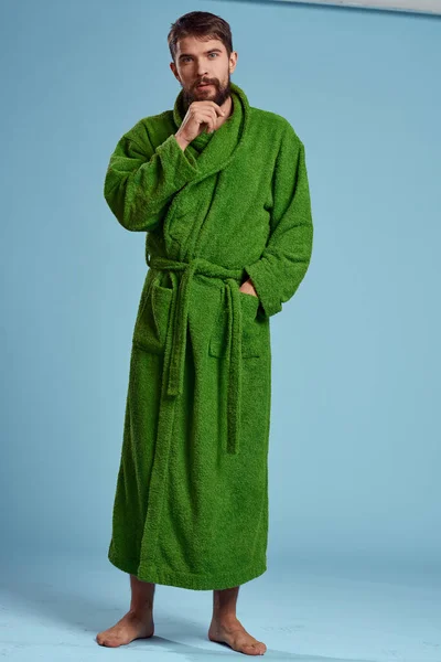 Чоловік в зеленому халаті в повному зростанні на синьому фоні з нетерпінням чекає — стокове фото