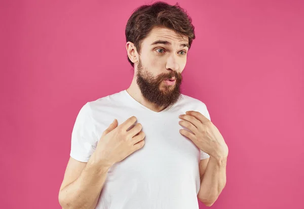 Um cara alegre com barba ri em um fundo rosa e gesticula com as mãos — Fotografia de Stock