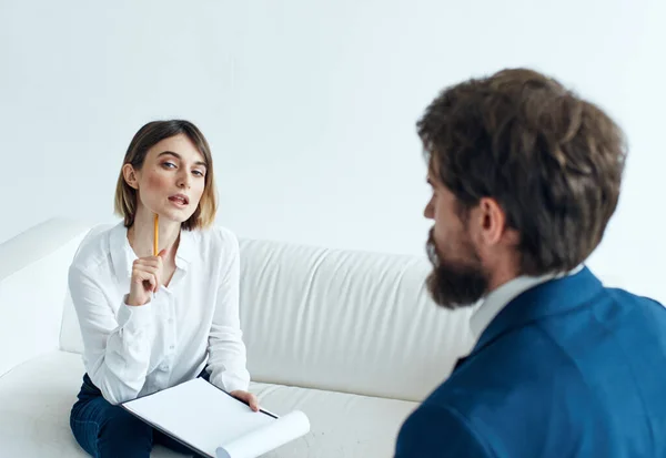 A man in a blue jacket and a beard talks to a woman on the sofa indoors — Stock Photo, Image