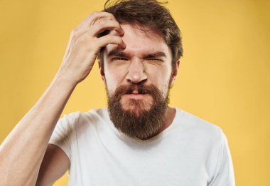 Sarı arka planda sakallı asabi genç bir adam.