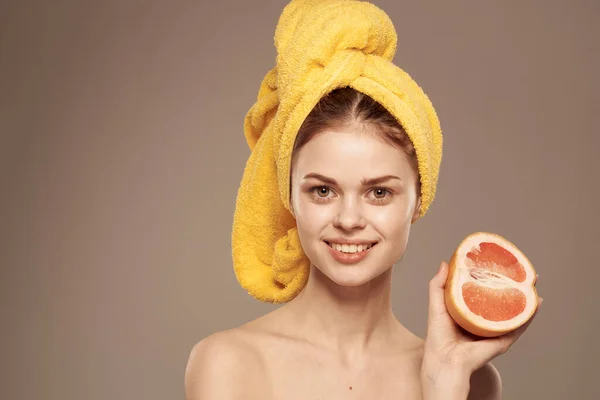 Mulher alegre com uma toalha amarela na cabeça ombros nus toranja na mão cosméticos naturais — Fotografia de Stock
