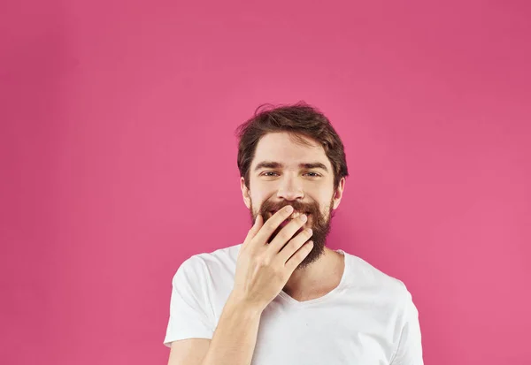 Щасливий молодий чоловік на рожевому тлі в білій футболці і товстої бородою жестикулювати руками — стокове фото