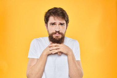 Beyaz tişörtlü bir adam el kol hareketleri yapar. Stüdyo tarzı sarı arka plan duyguları.