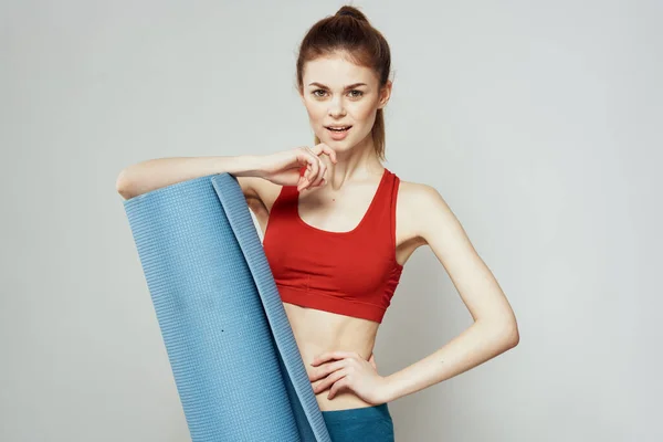 Mujer sostiene en la mano una alfombra para fitness deporte figura delgada ejercicios fondo claro — Foto de Stock