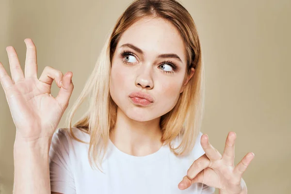 Mulher loira alegre em um branco gestos camiseta com suas emoções da mão fundo bege — Fotografia de Stock