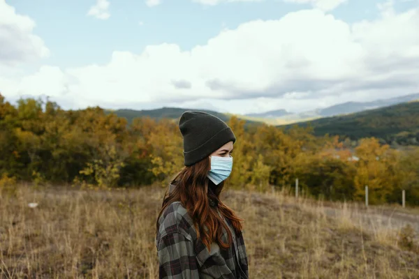 Mujer excursionista con gorra caliente con una máscara médica en su cara en el bosque — Foto de Stock