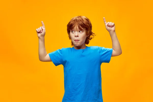 Een roodharige jongen in een blauw T-shirt wijst met zijn vingers omhoog en kijkt opzij — Stockfoto