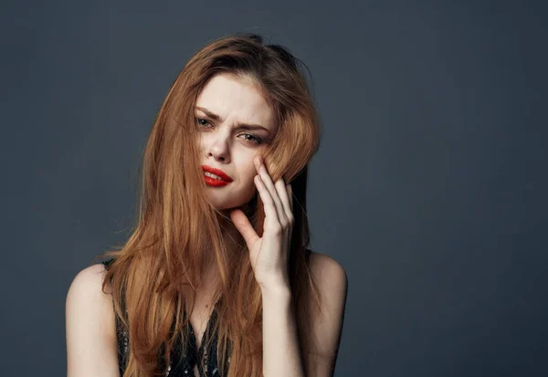 Mujer con los labios rojos y en un vestido negro sobre un fondo gris toca su cara con sus manos —  Fotos de Stock